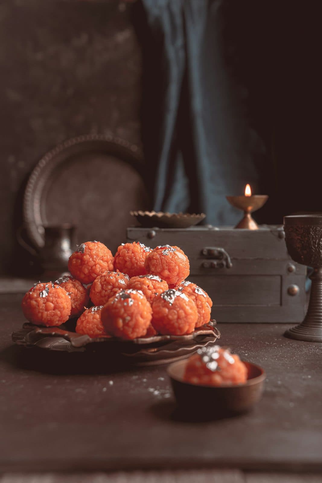 Boondi laddoos stacked on a plate beside a diya