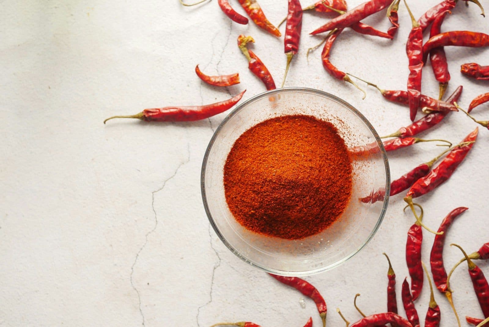 Kashmiri red chilli powder in a glass bowl with whole dry chillies
