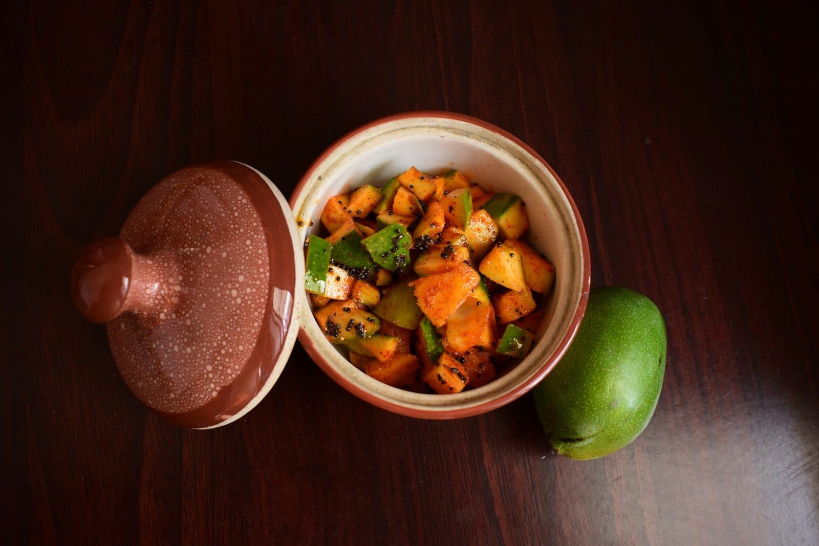 Mango pickle in a clay pot with a raw mango